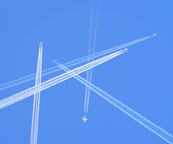 Many distant passenger jet planes flying on high altitude on clear blue sky leaving white smoke trace of contrail behind. Busy air transportation concept.
